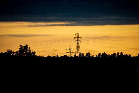 Countryside scene of fields and electricity pylons against the golden sunset sky - Powered by Adobe