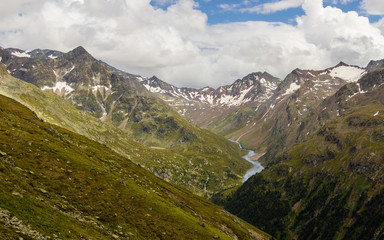 Valley in the Alps with snowy mountain peaks and a meandering water stream