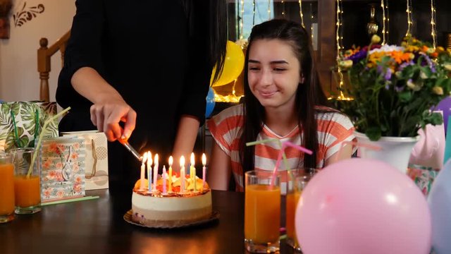 Happy teen girl with birthday cake at anniversary party. Lighting candles on birthday cake. People celebrating birthday concept. Slow motion 4k