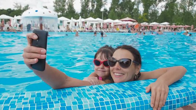 Family in the pool does selfie. Mom and daughter in the water park. A woman with a child is photographed in the swimming pool.
