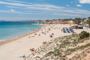 Sandy beach at the Mediterranean Sea on a summer day. Spanish beach with people sunbathing and swimming