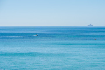 View of the blue water of the Mediterranean Sea with a boat and island on a summer day with clear sky