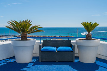 Wooden bench with two palm trees over the Mediterranean Sea with clear blue water in Campoamor