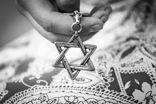 Young woman's hand holding a Star of David - Magen David key chain. The State of Israel, Holocaust remembrance, Judaism, Zionism concept image. Black and white image.