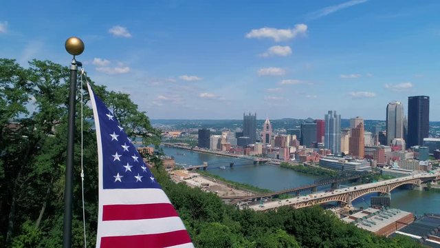 A lowering aerial view of an American flag on a flag pole above the Pittsburgh skyline on a summer day. As seen from Emerald View Park. Shot at 48fps for slow motion.  	
