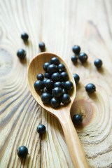 Fresh organic berries of black currant are in the rustic spoon on a wooden surface.