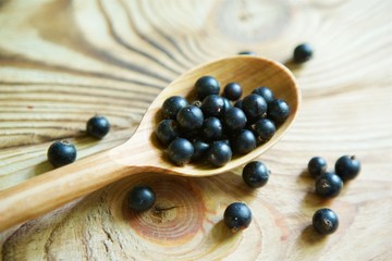 Fresh organic berries of black currant are in the rustic spoon on a wooden surface.