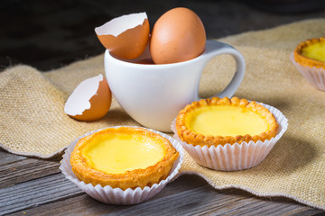 Egg tarts and eggs on burlap and wooden surface 