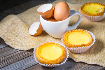 Egg tarts and eggs on burlap and wooden surface 