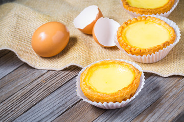 Egg tarts and eggs on burlap and wooden surface 