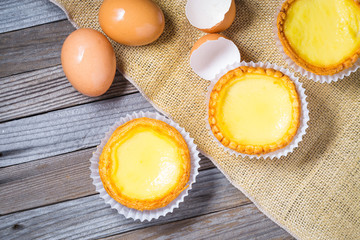 Egg tarts and eggs on burlap and wooden surface 