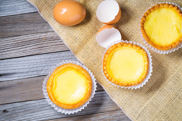 Egg tarts and eggs on burlap and wooden surface 
