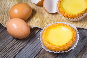 Egg tarts and eggs on burlap and wooden surface 