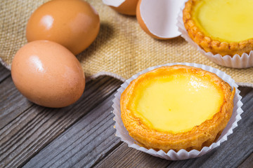 Egg tarts and eggs on burlap and wooden surface 