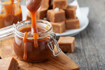 Homemade salted caramel sauce in jar on rustic wooden table. - obrazy, fototapety, plakaty