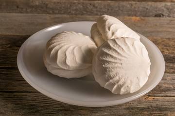 Three sweet marshmallows on a white plate on wooden background