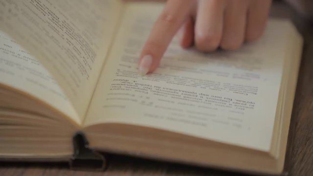 woman hand holds a book and moves her fingers along the page while reading education leisure reading paper