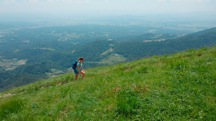 AERIAL: Flying over a fit young female hiking up a beautiful green mountain.