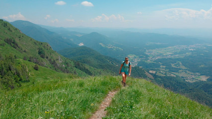 Fototapeta na wymiar AERIAL: Fit young female tourist hikes up a narrow mountain trail in the Alps.