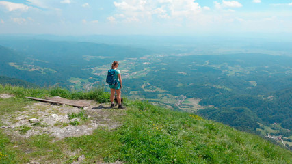 Fototapeta na wymiar AERIAL: Female tourist looking at green valley after hiking up a grassy mountain
