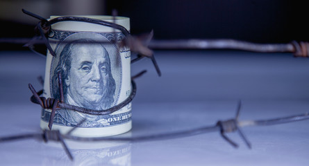 Economic warfare, sanctions and embargo busting concept. US Dollar money wrapped in barbed wire.