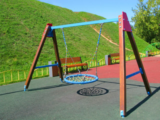 Obraz premium Hanging swings at childrens playground. Swings of modern design in the form of a nest with a wicker seat. Children's playground has an artificial soft covering.