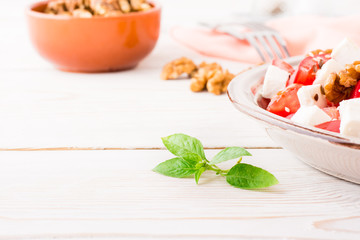 Fresh basil leaves on a background of vegetable salad in a plate on a white wooden table