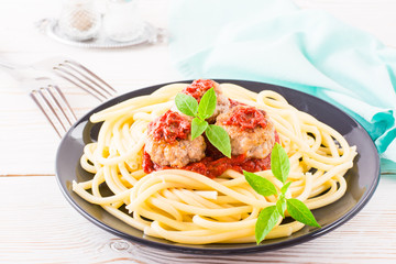 Spaghetti and meatballs in tomato sauce with fresh basil leaves on a plate on a table