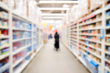 Blurred silhouette of a woman with a shopping cart in a supermarket. customer in the shop. Blurred rows of the supermarket.