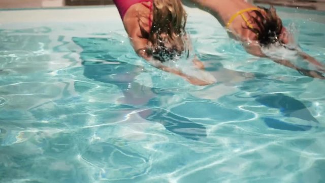 Women dive into pool on summer day, slow motion