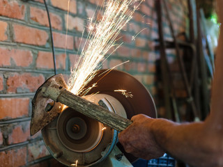 farmer sharpens garden tool on electric grindstone