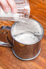 pouring flour from glass into steel sifter