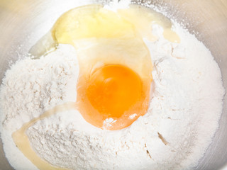 flour with broken egg close up in steel bowl