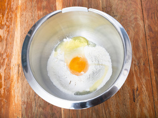 pile of flour with broken egg in steel bowl