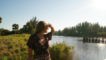 Young blonde woman happy and smiling searching in the horizon for a boat in a river in Florida, USA