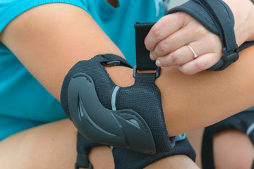Woman rollerskater putting on elbow protector pads on her hand
