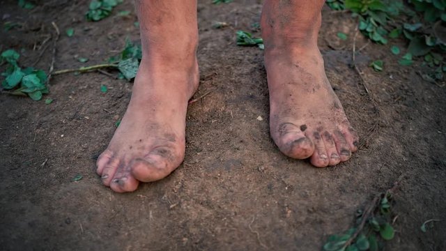 Close-up barefooted dirty feet of a child standing on a damp ground