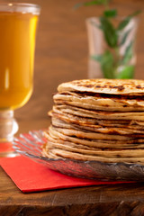 Fried round pancakes on a plate, drink in a glass, wooden background.