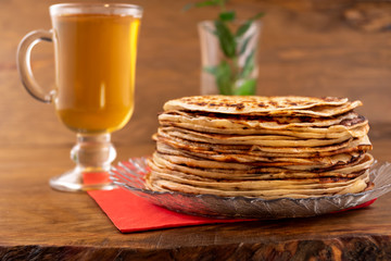 Delicious dessert of fried round pancakes and green tea in a glass, wooden background.