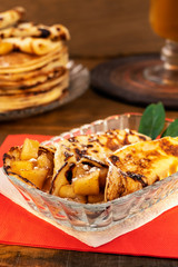 Rolls of pancakes with apple  filling in a glass plate on a red napkin, wooden background, vertical frame.