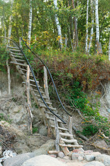 Stairs for descent to the sea. Wooden staircase with railing on the slope.