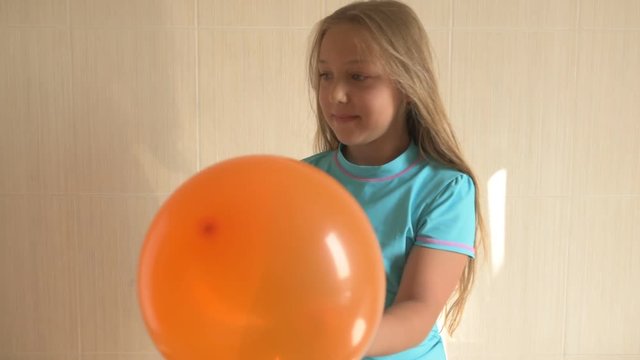 happy girl in a blue T-shirt blows bright balloon in bathroom at home. Blond boy with needle pierces a balloon. shallow focus