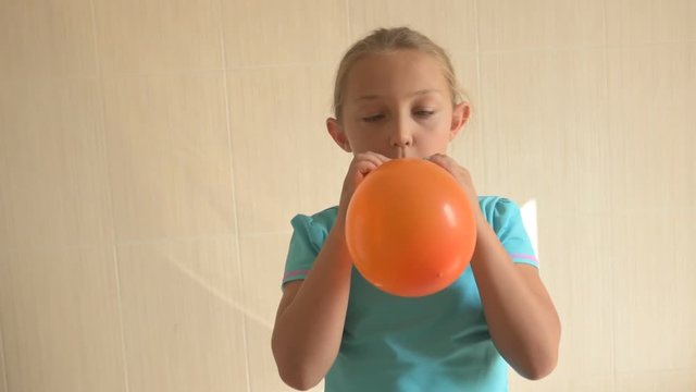 Happy girl in blue t-shirt inflates a bright orange ball in bathroom at home. Shallow focus