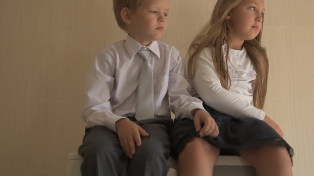 Back to school. Portrait of happy children with blue eyes and blond hair in school uniform. Boy and a preschool girl sitting on washing machine at home in bathroom. Shallow focus
