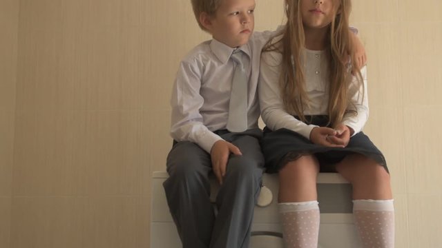 Back to school. Portrait of happy children with blue eyes and blond hair in school uniform. Boy and a preschool girl sitting on washing machine at home in bathroom. Shallow focus
