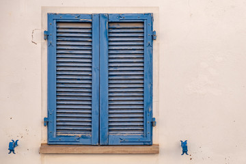 Fototapeta na wymiar The window is covered with blue wooden shutters on the facade of the beige house
