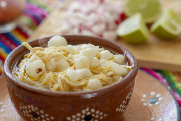 Pozole blanco con pollo, acompañado con rábanos, limones y tostadas en fondo de colores mexicanos