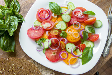 Sliced heirloom tomatoes, crisp cucumbers with chopped red onion, chives drizzled with olive oil and added basil leaves.