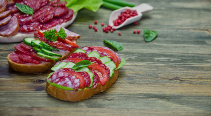salami sandwich with tomatoes and cucumbers next sliced salami and tomato and Basil leaves with salad on wooden background 