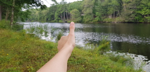 right Human hand with thumbs up gesture in nature next to a river